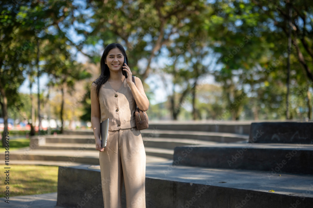 Fototapeta premium Young woman walking and talking on phone in park