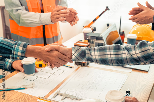 Partner and contractor concept of construction team shaking hands greeting new project start plan, project contract in office center at construction site.