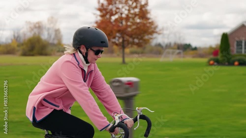 Woman cycling outdoors on a rural road while wearing a helmet and pink jacket