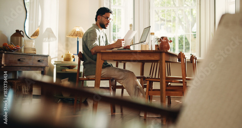 Reading, paperwork and man with laptop, confused and freelance contract for design project and home. Review, clause and person with documents for remote work, graphic designer and puzzled in house