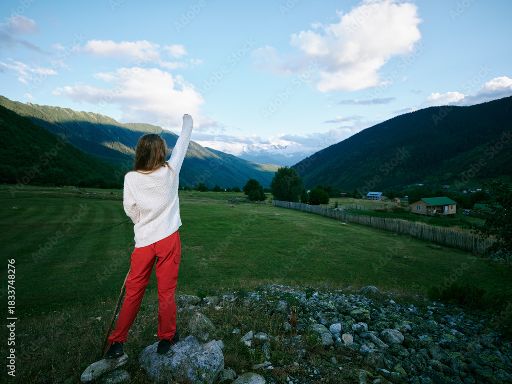 Obraz premium Woman standing on a rocky overlook in open countryside, arms raised toward distant mountains and valley, clear blue sky, vibrant landscape, feeling freedom and exploration