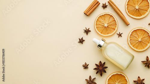 Flat lay of a cosmetic serum dropper bottle with dried orange slices, cinnamon sticks, and star anise on a beige background.