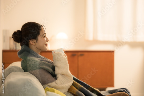 Fotografie 夜の灯りの部屋でホットドリンクを飲む若い女性　女性の冬イメージ　白熱灯のあたたかいイメージ