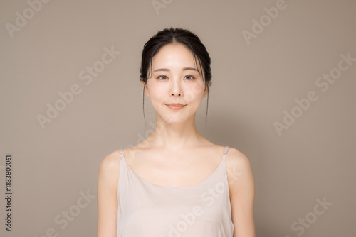 髪の毛がアップ背景がベージュの使いやすい美容やスキンケアの美しい女性のイメージ上半身正面カメラ目線