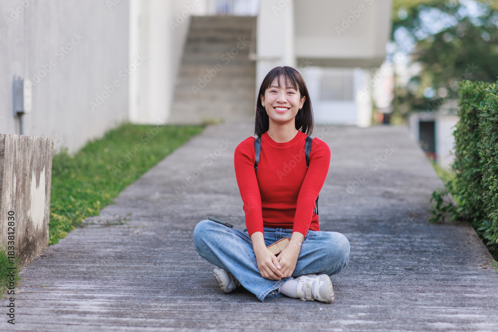 Fototapeta premium Happy asian student smiling sitting casually on campus path