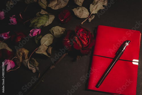Dried red rose, notebook, pen symbolizing lost love