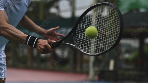 A tennis player swings the racket toward a fast-moving ball, captured in a dynamic close-up action shot on the court