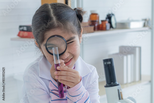 Cute Arabian girl elementary student kid wearing lab coat standing near microscope hold glass magnifier looking at camera in laboratory classroom, lifestyle learning education science class scientist