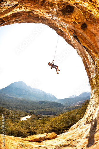 A girl rock climber. A rock climber hangs on a rope against the backdrop of the sky and beautiful mountains. The girl descends after completing a climbing route.