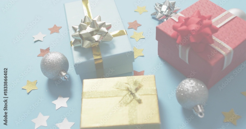 Fototapeta premium Showing three wrapped gift boxes sitting on pale blue table, with metallic bows and silver baubles