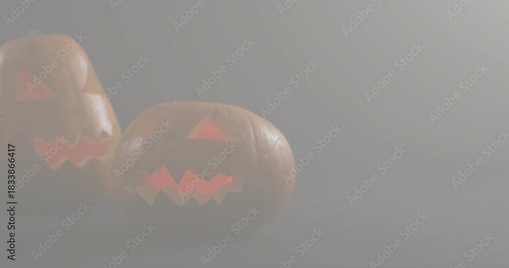 Obraz premium Glowing carved pumpkins emitting warm orange light in dim foggy studio on matte surface, copy space