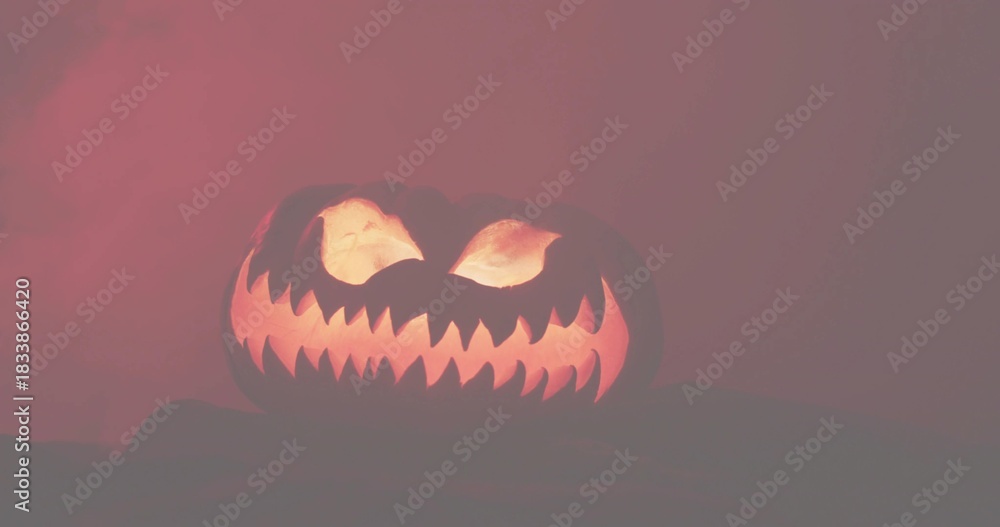 Naklejka premium Glowing carved pumpkin revealing jagged teeth on tabletop, with internal light and dark cloth