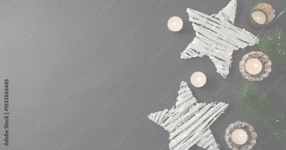 Fototapeta premium Showing display at right on gray tabletop with white woven stars, lit votives, garland, copy space