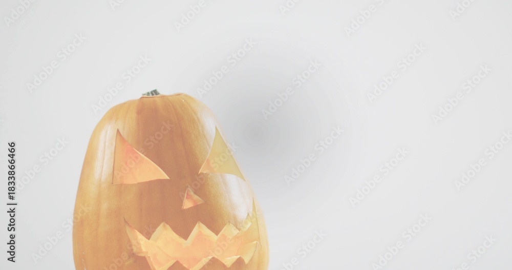 Fototapeta premium Sitting carved pumpkin emitting warm light on studio tabletop, with stem, faint shadow, copy space