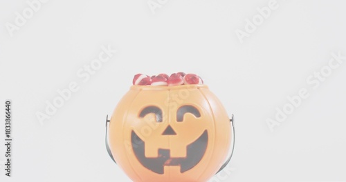 Displaying orange jack-o'-lantern bucket sitting on white tabletop, showing candies and molded face