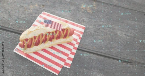 Fototapeta Sitting hot dog on picnic table, with American flag toothpick and blue overlay, copy space
