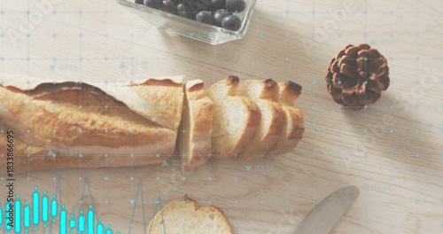 Showing sliced baguette lying on wooden table, with berry bowl, pinecone, knife, turquoise overlay