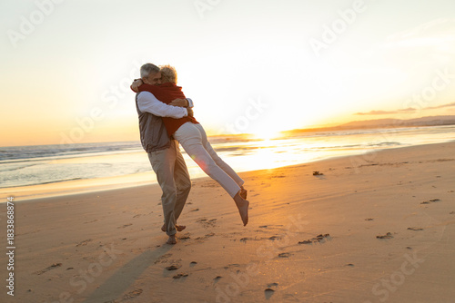 Senior couple embracing, having fun playing on beach at sunset