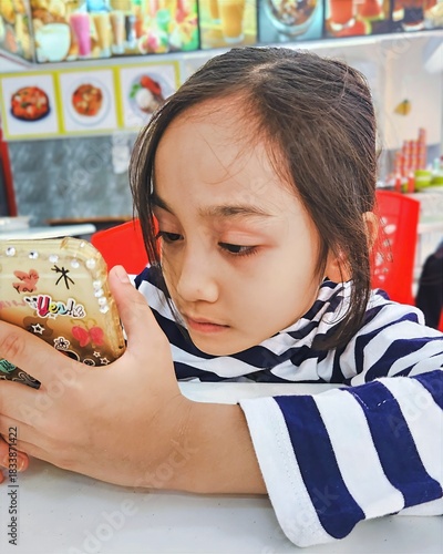 Malaysia, Bangi - September 7, 2024 Little girl using mobile phone at the restaurant.