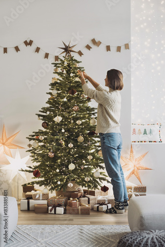 Young woman decorating Christmas tree at home, winter holiday and xmas time concept