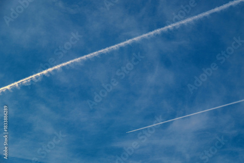 Plane trail and white clouds in the blue sky. Chemtrail conspiracy theory.