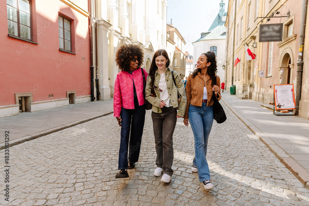 Naklejka premium A group of three female friends walking and laughing while two of them hold hands