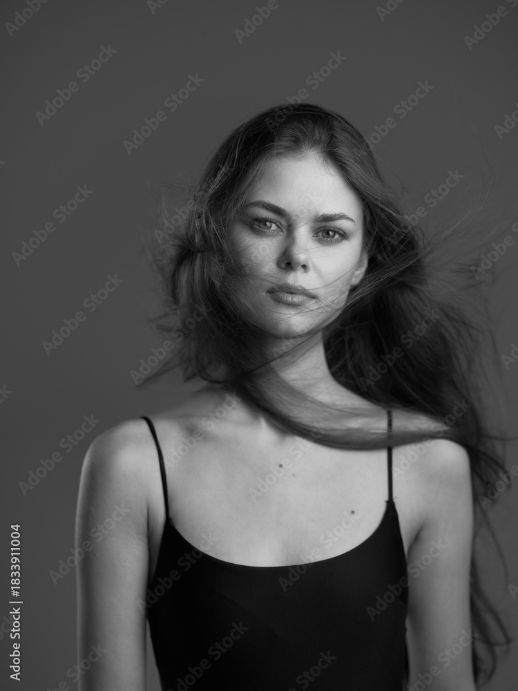 Fototapeta premium Black and white portrait of a young woman with loose hair wearing a black sleeveless top looking calm and confident