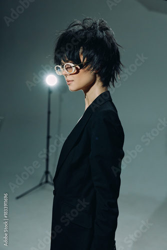 Stylish woman with short hair wearing white glasses and black blazer in minimalistic studio lighting