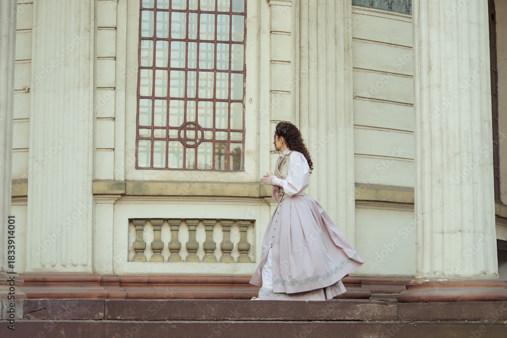 Fototapeta premium An elegant woman in a vintage dress stands by an old stone column