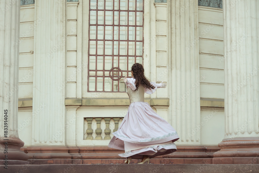 Fototapeta premium An elegant woman in a vintage dress stands by an old stone column