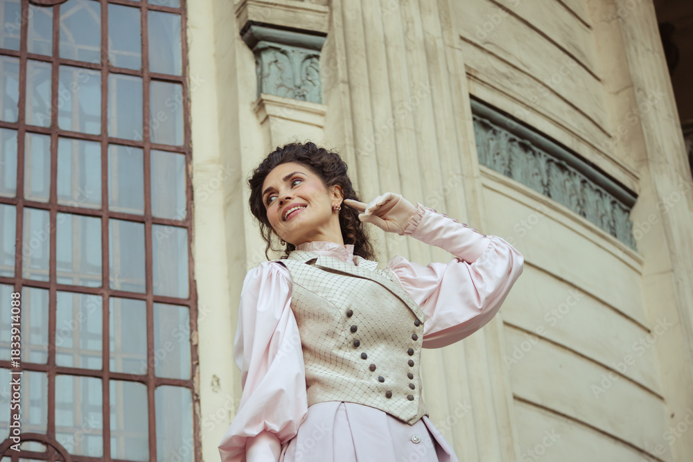 Fototapeta premium An elegant woman in a vintage dress stands by an old stone column