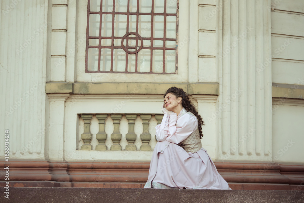 Fototapeta premium An elegant woman in a vintage dress stands by an old stone column