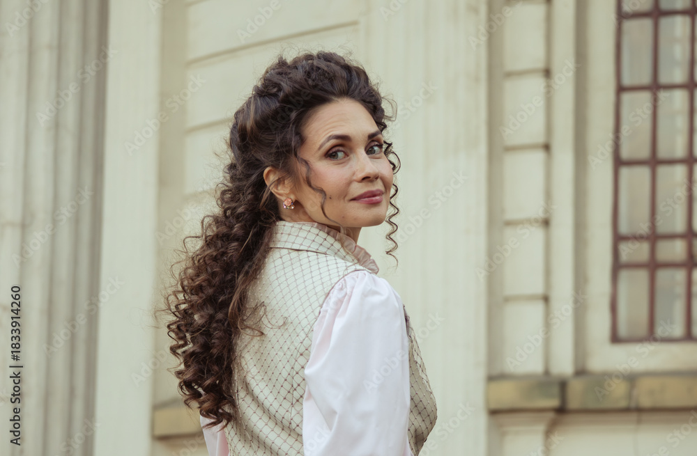Fototapeta premium An elegant woman in a vintage dress stands by an old stone column