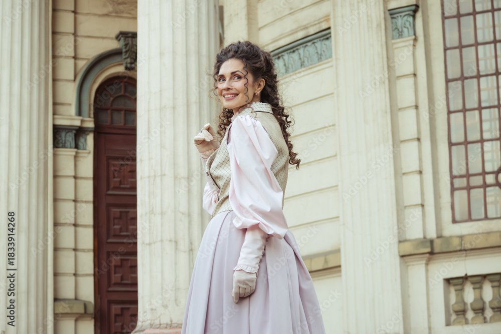Fototapeta premium An elegant woman in a vintage dress stands by an old stone column