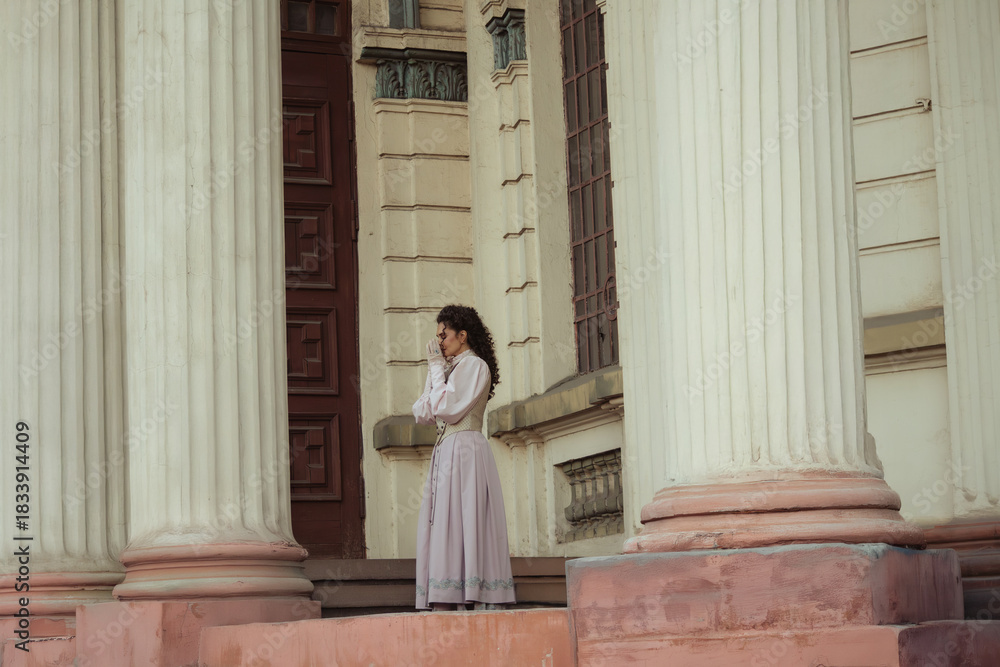 Fototapeta premium An elegant woman in a vintage dress stands by an old stone column