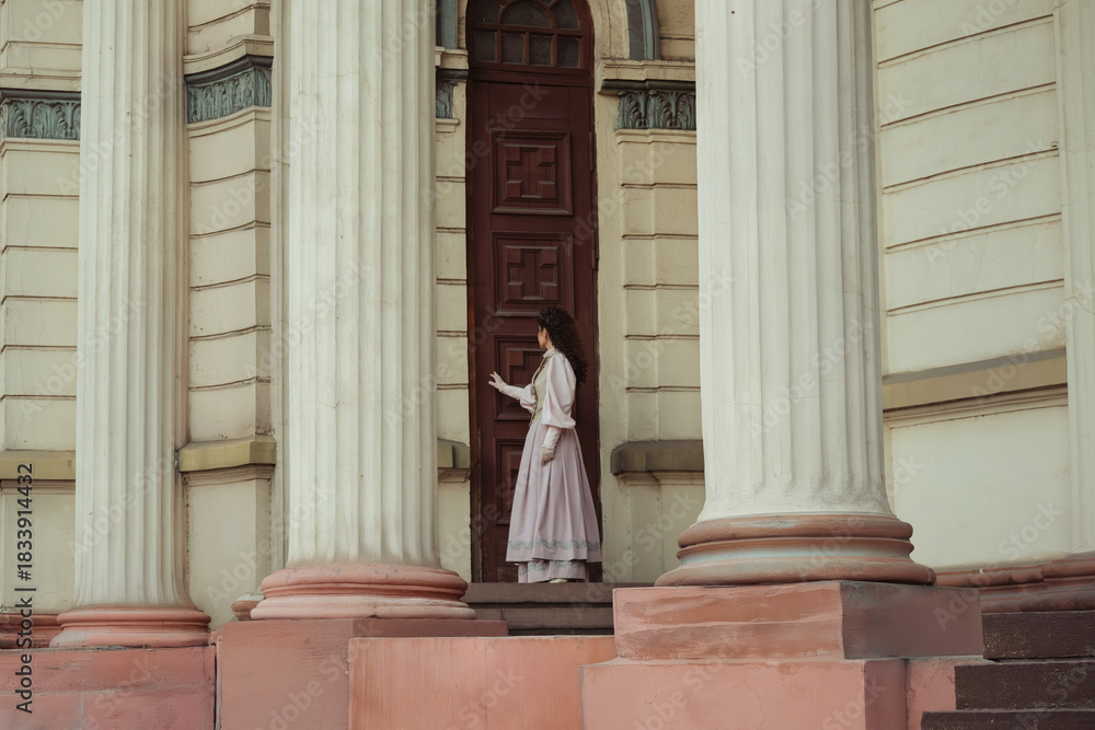 Fototapeta premium An elegant woman in a vintage dress stands by an old stone column
