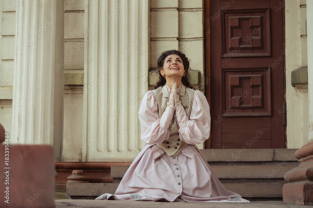 Fototapeta premium An elegant woman in a vintage dress sits next to an old stone column with a very happy expression on her face.