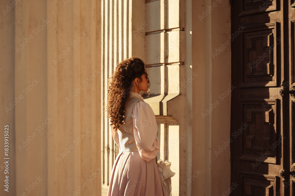 Fototapeta premium An elegant woman in a vintage dress stands by an old stone column
