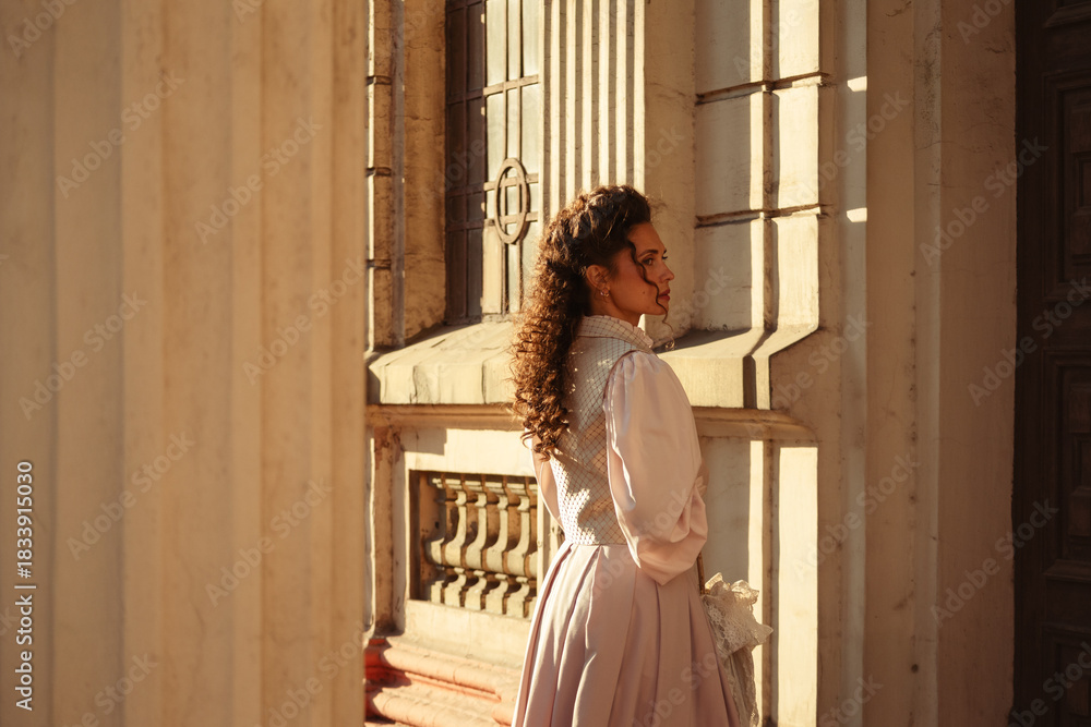 Obraz premium An elegant woman in a vintage dress stands by an old stone column