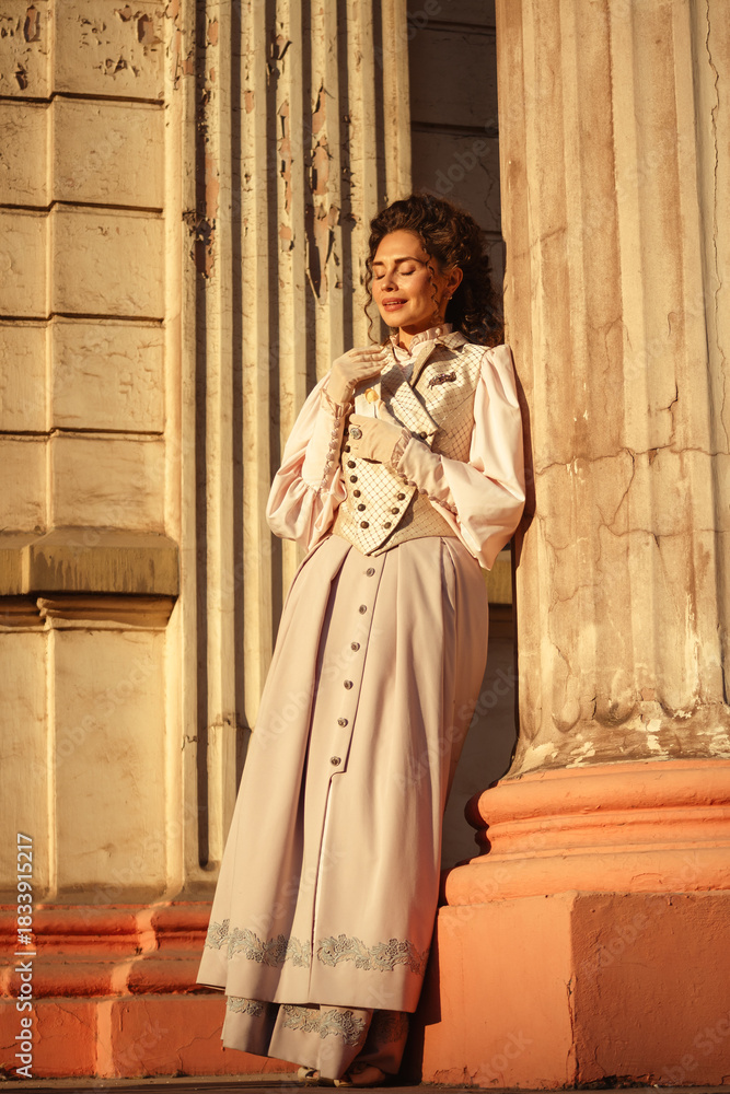 Fototapeta premium An elegant woman in a vintage dress stands by an old stone column