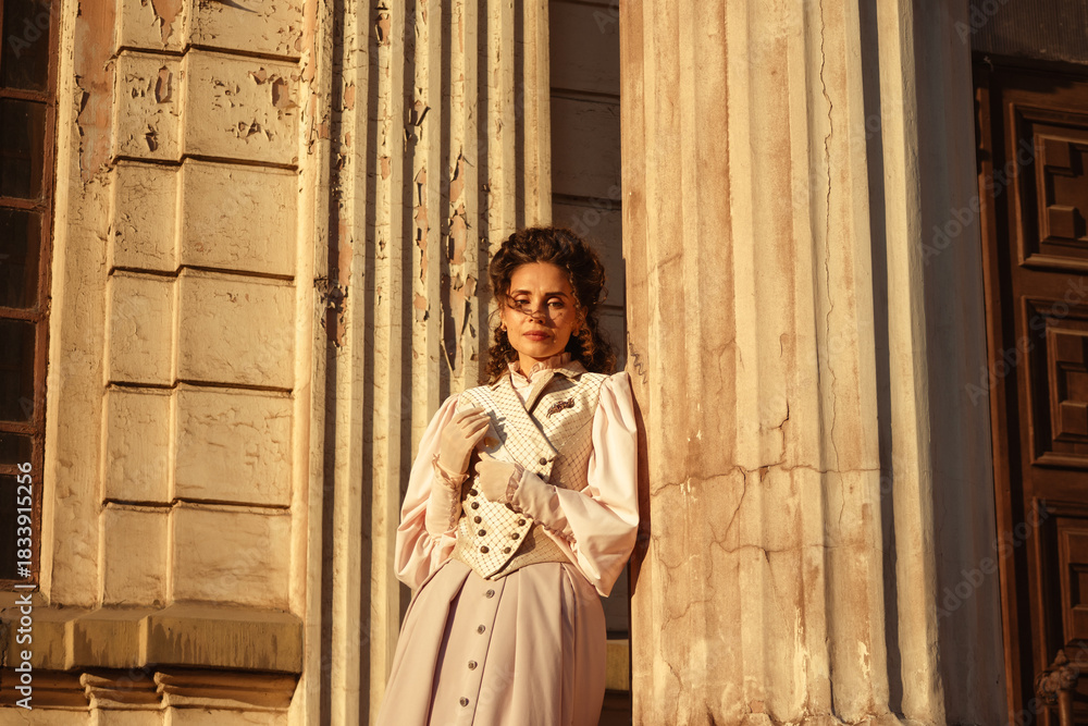 Fototapeta premium An elegant woman in a vintage dress stands by an old stone column