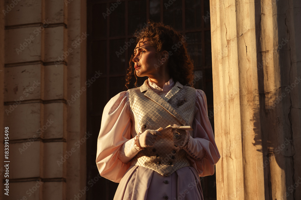 Fototapeta premium Portrait of a woman in vintage clothing, illuminated by warm sunlight, against a backdrop of ancient architecture.