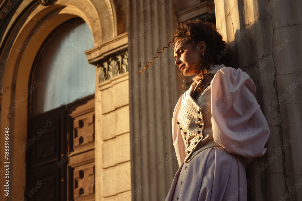 Obraz premium Portrait of a woman in vintage clothing, illuminated by warm sunlight, against a backdrop of ancient architecture.