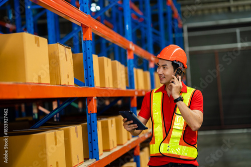 A man in a safety vest is talking on a cell phone while standing in a warehouse