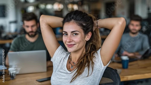 Confident woman leans back with a relaxed smile at a busy coworking space while colleagues work now