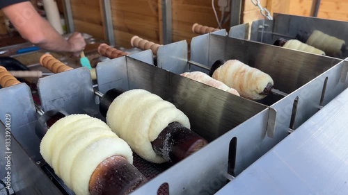Close-up chimney cakes grilling over hot coals, traditional Hungarian pastry turning on wooden spits, christmas market
