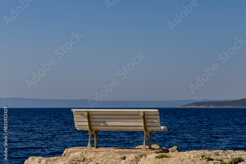 Fototapeta Naklejka Na Ścianę i Meble -  A bench overlooking the sea on a rocky shore near a walking path. Adriatic Sea, Makarska, Croatia.