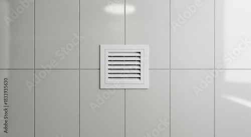White plastic air vent cover mounted on a glossy tiled wall. Bathroom ventilation grille close up. HVAC exhaust fan system for home interior