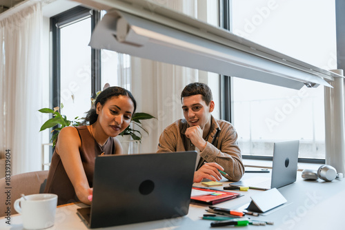 Female and male employees smiling and looking at laptop while sitting at desk