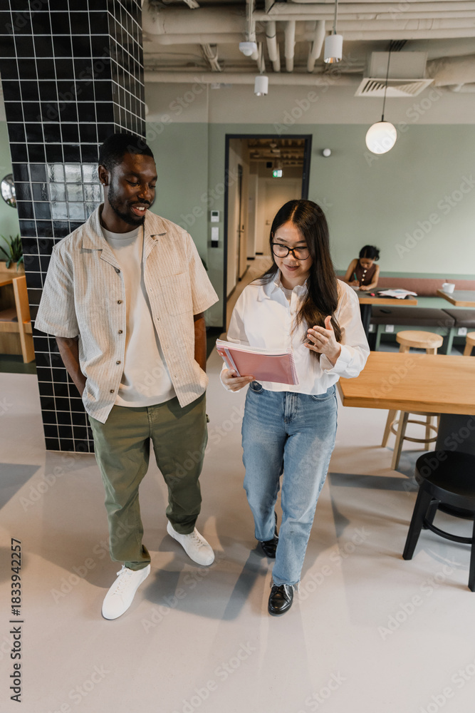 Obraz premium A man and a woman worker walk and read a notebook she is holding and talk while he smiles